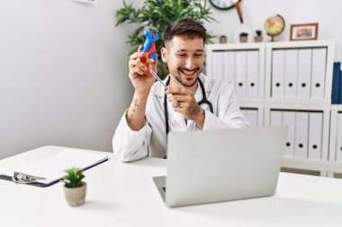 Doktor üniforması giyen genç İspanyol adam klinikte telekonksiyon yapıyor.