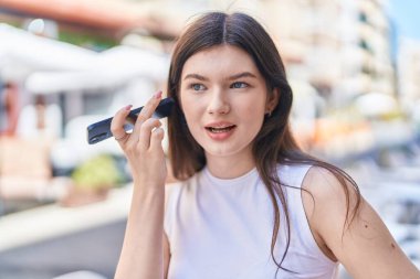 Beyaz kadın gülümsüyor. Caddedeki akıllı telefondan kendine güvenen sesli mesaj dinliyor.