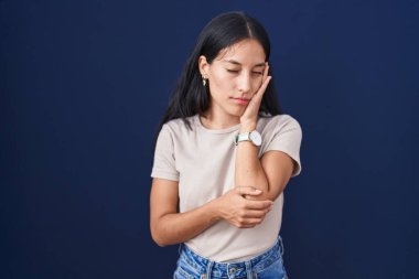 Mavi arka planda duran genç İspanyol kadın çapraz kollu depresyon sorunlarından yorgun ve sıkılmış göründüğünü düşünüyor.. 