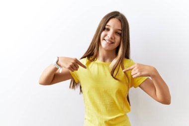 Genç esmer kız izole bir arka planda ayakta duruyor. Yüzünde bir gülümsemeyle, gururlu ve mutlu bir şekilde kendini işaret ediyor.. 