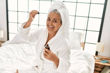 Yatak odasındaki yatakta serumu kullanan orta yaşlı gri saçlı kadın..