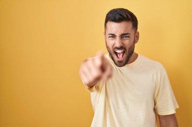 Sarı arka planda dikilen yakışıklı İspanyol adam kameraya kızgın ve sinirli bir şekilde bakıyor. 