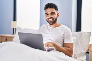 Yatak odasında dizüstü bilgisayar kullanan genç bir İspanyol.