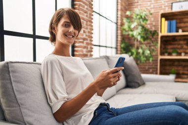 Evdeki kanepede oturan akıllı telefon kullanan genç, güzel İspanyol kadın.