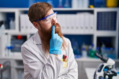 Young redhead man scientist sitting with doubt expression at laboratory