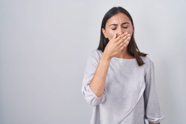 Young hispanic woman standing over white background bored yawning tired covering mouth with hand. restless and sleepiness. 