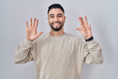 Soyutlanmış arka planda duran yakışıklı genç adam dokuz numarayı gösteriyor ve gülümserken kendinden emin ve mutlu.. 