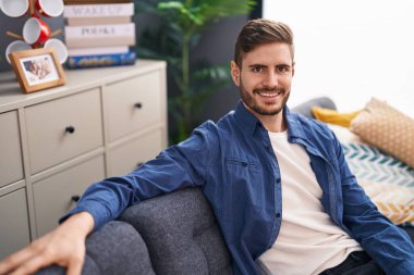 Evdeki koltukta kendinden emin gülümseyen beyaz bir genç.