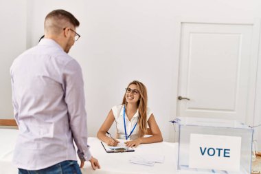 Genç seçmen seçim masasında duruyor ve seçim merkezinde siyasi parti işçisiyle konuşuyor..