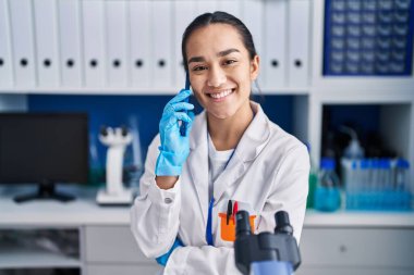 Laboratuvarda çalışan Latin asıllı genç bilim kadını akıllı telefondan konuşuyor.