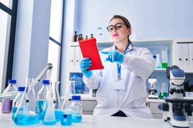 Young beautiful hispanic woman scientist using touchpad at laboratory