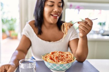 Hispanic brunette woman eating spaghetti at the kitchen