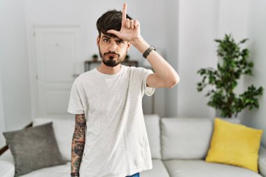 Oturma odasında sakallı İspanyol bir adam. Alnında parmakları olan insanlarla dalga geçiyor. Ezik hareketler yapıyor.. 