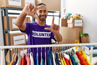 African american man wearing volunteer t shirt at donations stand smiling making frame with hands and fingers with happy face. creativity and photography concept. 