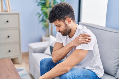 Evdeki kanepede oturan genç bir Arap omuz sakatlığı çekiyor.