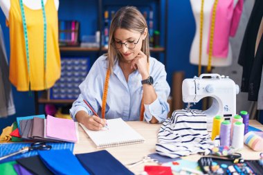 Young beautiful hispanic woman tailor smiling confident drawing on notebook at clothing factory