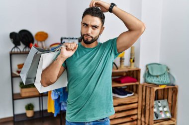 Satış mağazasında sakallı, alışveriş torbası tutan yakışıklı genç adam kafası karışıyor ve soru soruyor. Şüpheyle kararsız, kafa kafaya düşünerek. Düşünceli kavram. 