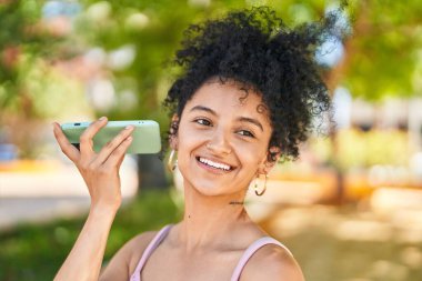 Young hispanic woman smiling confident listening audio message by the smartphone at park