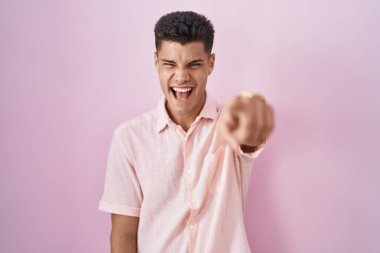 Genç İspanyol bir adam pembe arka planda dikiliyor. Kameraya kızgın ve sinirli olduğunu gösteriyor. 