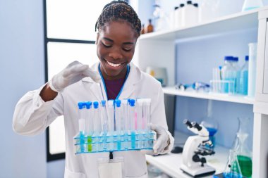 African american woman wearing scientist uniform holding test tubes at laboratory