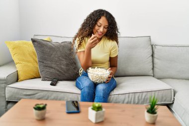 Evde patlamış mısır yiyen kendine güvenen genç Latin kadın.