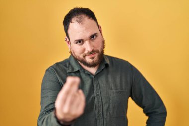 Plus size hispanic man with beard standing over yellow background doing italian gesture with hand and fingers confident expression 