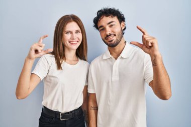 Gündelik giysiler giyen genç bir çift gülümseyerek ve el hareketleriyle hareket ederek parmaklarıyla işaret yapıp kameraya bakıyor. ölçüm kavramı. 