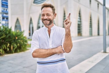 Şehrin dışındaki orta yaşlı adam kameraya bakıp gülümseyen ve zafer işareti yapan. İki numara.. 