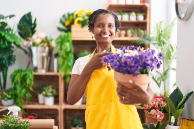 African woman with dreadlocks working at florist shop holding plant smiling happy pointing with hand and finger 
