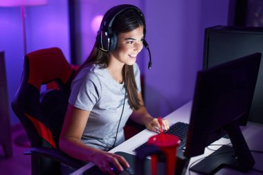 Young beautiful hispanic woman streamer playing video game using computer at gaming room