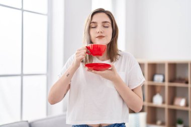 Young woman drinking coffee standing at home