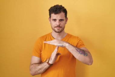 İspanyol asıllı genç adam sarı arka planda duruyor. Elleriyle hareket ediyor, hayal kırıklığına uğramış ve ciddi bir yüz ifadesi takınıyor. 