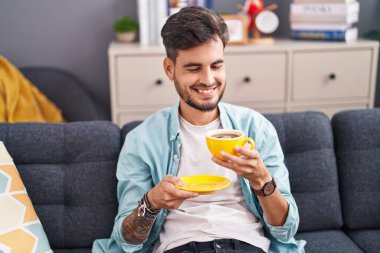 Genç İspanyol adam evdeki kanepede kahve içiyor.