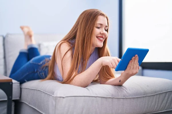 Młoda Ruda Kobieta Pomocą Touchpad Leżącego Kanapie Domu — Zdjęcie stockowe