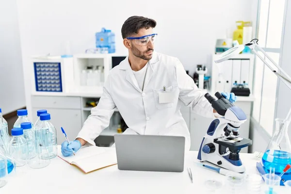 Mikroskop ve laptopla laboratuvarda bilimsel olarak çalışan yakışıklı bir İspanyol.