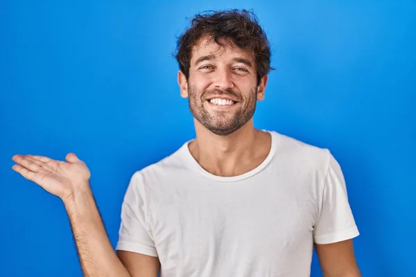 Joven Hispano Pie Sobre Fondo Azul Sonriendo Alegre Presentando Señalando —  Fotos de Stock