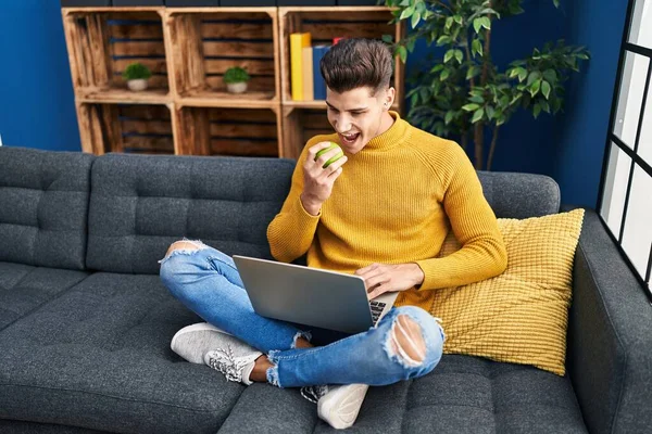 Young Hispanic Man Using Laptop Eating Apple Home —  Fotos de Stock