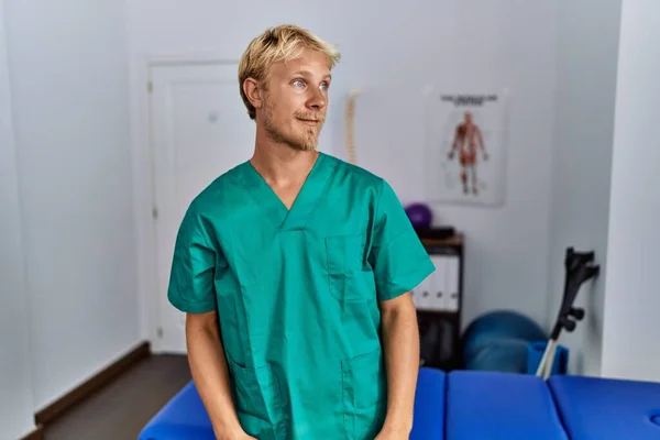 Young Blond Man Wearing Physiotherapist Uniform Standing Clinic Looking Away — Stockfoto
