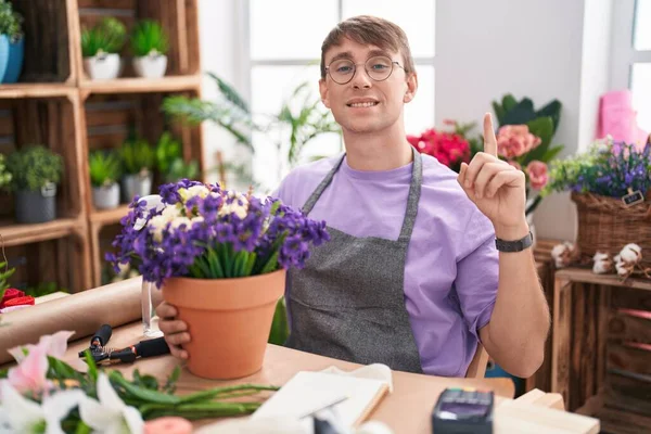 Caucasian blond man working at florist shop smiling amazed and surprised and pointing up with fingers and raised arms. 