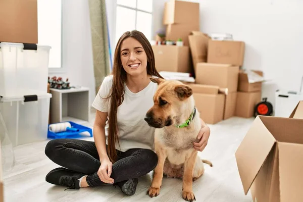 Young hispanic woman smiling confident hugging dog sitting on floor at new home