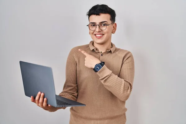 Non binary person using computer laptop cheerful with a smile on face pointing with hand and finger up to the side with happy and natural expression