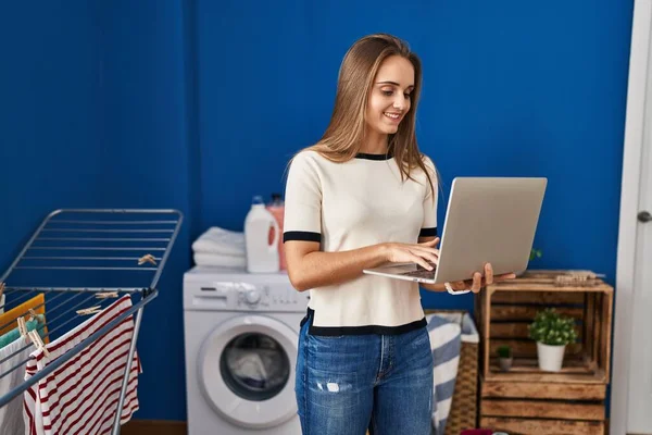 Çamaşır Odasında Dizüstü Bilgisayar Kullanan Kendine Güvenen Genç Sarışın Kadın — Stok fotoğraf