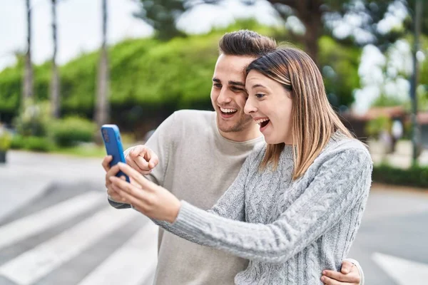 Man and woman couple hugging each other using smartphone at street