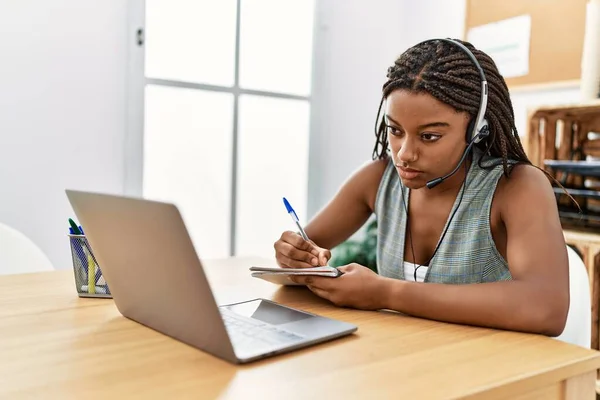 年轻的非洲裔美国妇女呼叫中心代理人在办公室的笔记本上写字 — 图库照片
