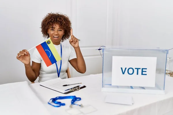 Young african american woman at political campaign election holding venezuela flag surprised with an idea or question pointing finger with happy face, number one