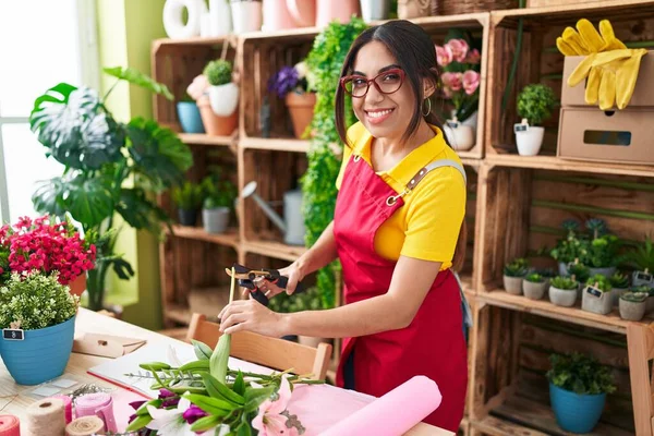 Young beautiful arab woman florist cutting plant at flower shop