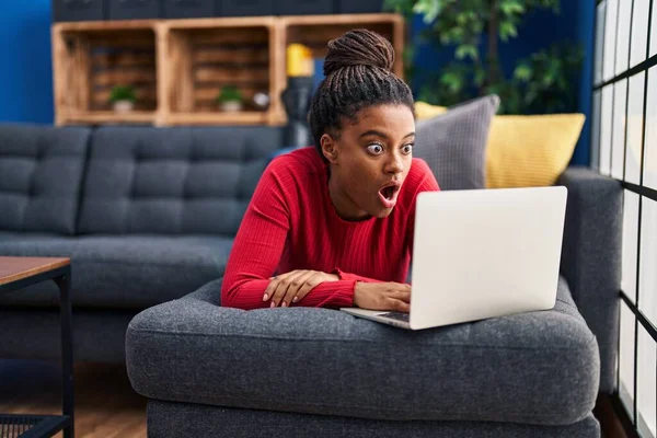 Örgülü, bilgisayar laptopu kullanan, ağzı açık, korkmuş ve şaşırmış genç bir Afro-Amerikalı. 