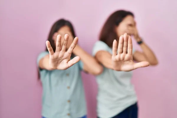 Young mother and daughter standing over pink background covering eyes with hands and doing stop gesture with sad and fear expression. embarrassed and negative concept.