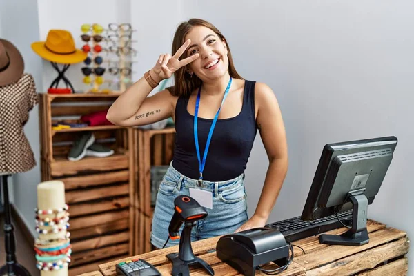 Genç esmer kadın perakende dükkanında açık metinlerle pankart tutuyor. Barış sembolü yapıyor. Yüzünde parmakları var. Gülümsüyor. 