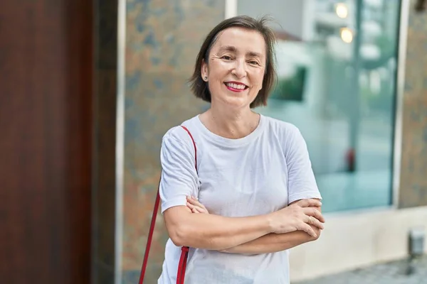 Middle age woman standing with arms crossed gesture at street